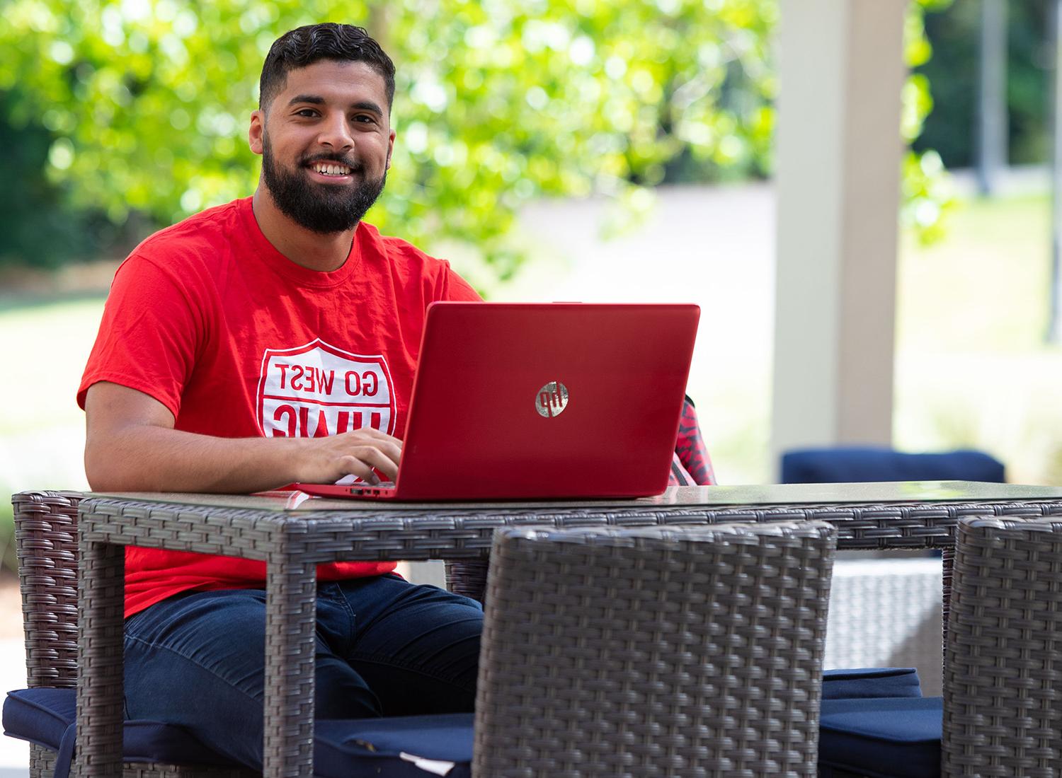 male student working on a laptop on the Campus Center Back Patio